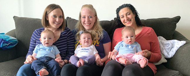 Three women sit on a sofa, each with a baby on her lap